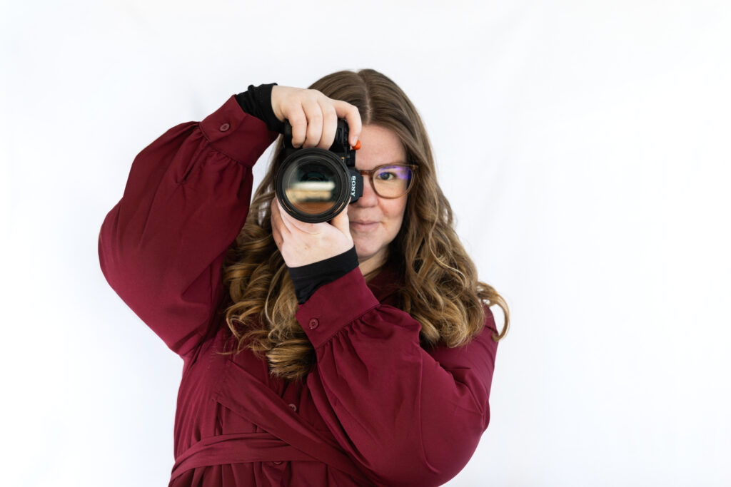jonge vrouw voor een witte achtergrond met een camera in haar handen die ze voor een oog houd