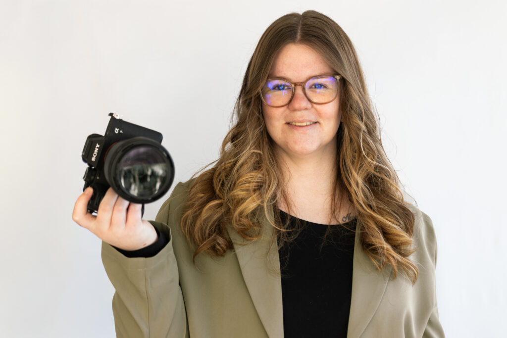 jonge vrouw met blond haar houdt een camera vast en lacht naar de camera